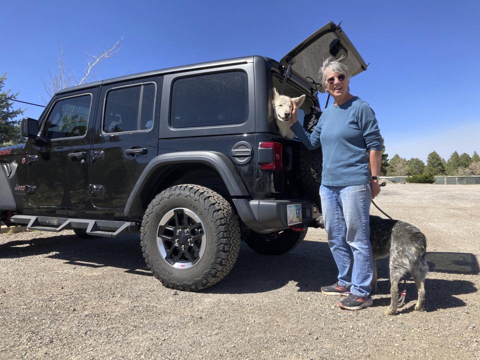 Lisa Wells, stands with her dogs Lily, and Bandit, as they wait for family in the parking lot on the outskirts of Flagstaff, Ariz., on Wednesday, April 20, 2022. Wells and her family evacuated because of a wildfire that destroyed their home. (AP Photo/Felicia Fonseca)