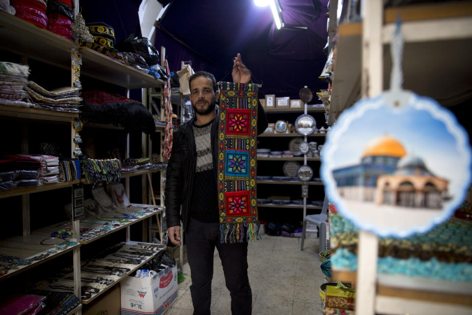 In this Wednesday, Feb. 12, 2020 photo, Palestinian shopkeeper Abdelkarim al-Karaki poses for a photo in his store, which carries souvenirs by artisans engaged in traditional handicrafts, but about half the products in his shop come from China, including refrigerator magnets with pictures of Jerusalem and embroidered wall hangings, in the West Bank city of Hebron. The local market has long been flooded by low-cost Chinese goods. Traders fear that if the outbreak and quarantine efforts continue they will have to switch to more expensive alternatives, passing higher prices onto consumers who may not be able to bear them. (AP Photo/Majdi Mohammed)