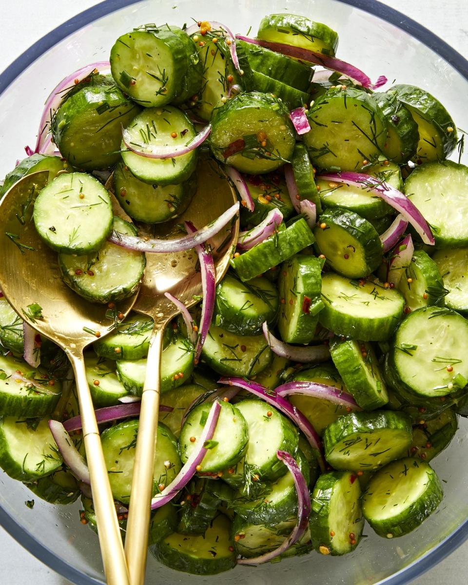 a salad bowl filled with sliced cucumber rounds and thinly sliced raw red onion tossed in a dressing made with whole mustard seeds and chopped fresh dill and chives