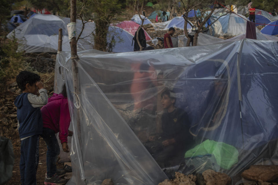 In this Wednesday, Sept. 25, 2019 photo Syrians stand inside their makeshift tent near the refugee and migrant camp at the Greek island of Samos. Greece's conservative government announced Wednesday Nov. 20, 2019, plans to overhaul the country's migration management system, and replacing existing camps on the islands with detention facilities and moving and 20,000 asylum seekers to the mainland over the next few weeks. (AP Photo/Petros Giannakouris)