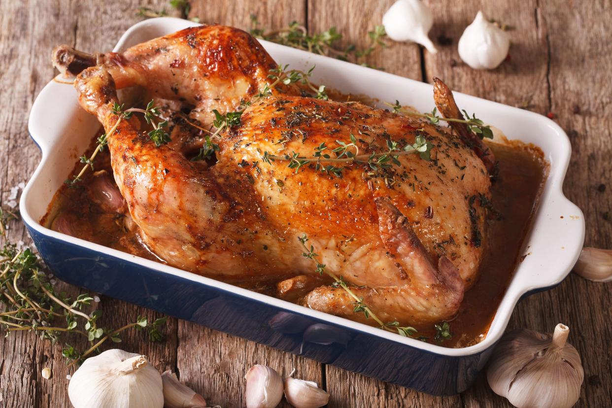 Whole roast chicken with vegetables in a blue ceramic cooking pot on a wooden table with garlic cloves