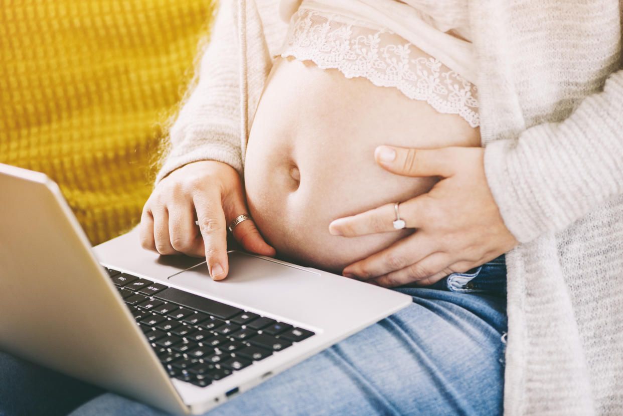 Pregnant mother holds stomach while typing at at laptop. Two women have spoken to Yahoo Canada about struggling financially during maternity leave. (Getty Images) (Getty Images)