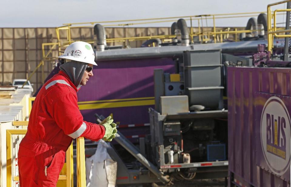 In this March 25, 2014 photo, a worker watches over a hydraulic fracturing operation at an Encana Corp. gas well near Mead, Colo. In the background is a tall canvas wall around the perimeter of the extraction site, which mitigates noise, light and dust coming from the operation during the drilling and completion phase, which generally takes a few weeks. (AP Photo/Brennan Linsley)