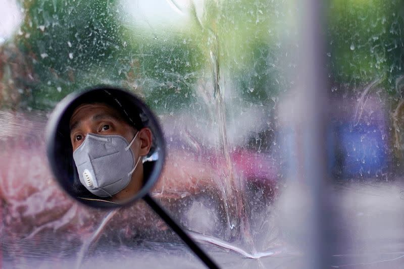 A man wearing a face mask is seen reflected on her electric bike's rearview mirror on a street after the lockdown was lifted in Wuhan