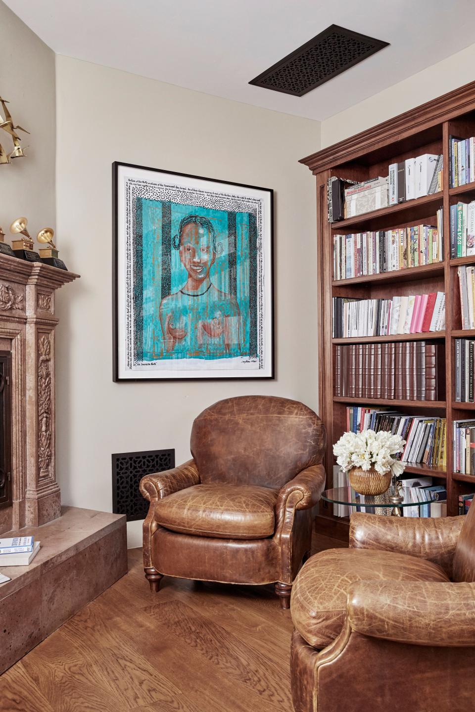 The library features a cozy nook with leather club chairs from Acquisitions by Henredon, custom-made cherry cabinets, and a hand-carved travertine fireplace. The art is The Sovereign People by Tony Ramos.