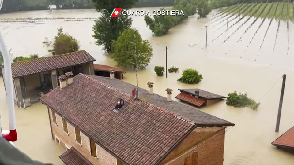 This photo provided by the Italian Coast guard shows a man on the roof of a flooded house just before being rescued by helicopter, in the area of the town of Faenza in the northern Italian region of Emilia Romagna, Wednesday, May 17, 2023. Unusually heavy rains have caused major floodings in Emilia Romagna, where trains were stopped and schools were closed in many towns while people were asked to leave the ground floors of their homes and to avoid going out. (Guardia Costiera via AP)