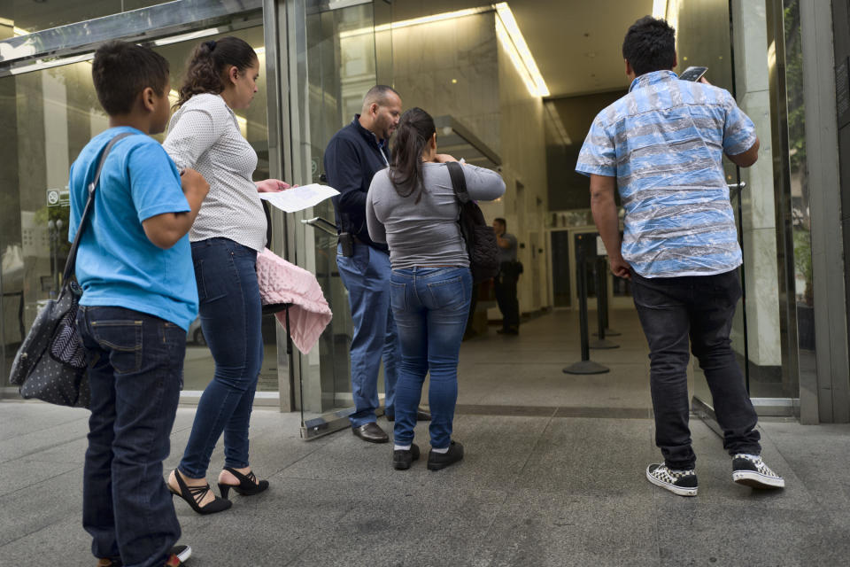 In this May 30, 2019 photo immigrant families show paperwork to enter an immigration court in an office building in downtown Los Angeles. U.S. authorities are fast-tracking families' cases through the immigration courts in a pilot program aimed at discouraging many from making the journey to seek refuge in the United States. (AP Photo/Richard Vogel)