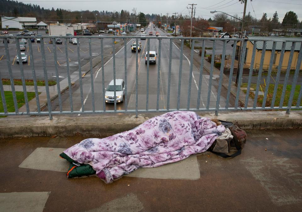 A person sleeps on a pedestrian bridge over West 18th Avenue in Eugene on the same day that Gov. Tina Kotek announced plans she hopes will help alleviate the homeless crisis in Oregon.