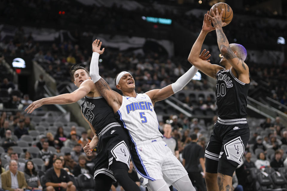 Orlando Magic's Paolo Banchero (5) tangles with San Antonio Spurs' Jeremy Sochan (10) and Zach Collins under the basket during the first half of an NBA basketball game, Tuesday, March 14, 2023, in San Antonio. (AP Photo/Darren Abate)