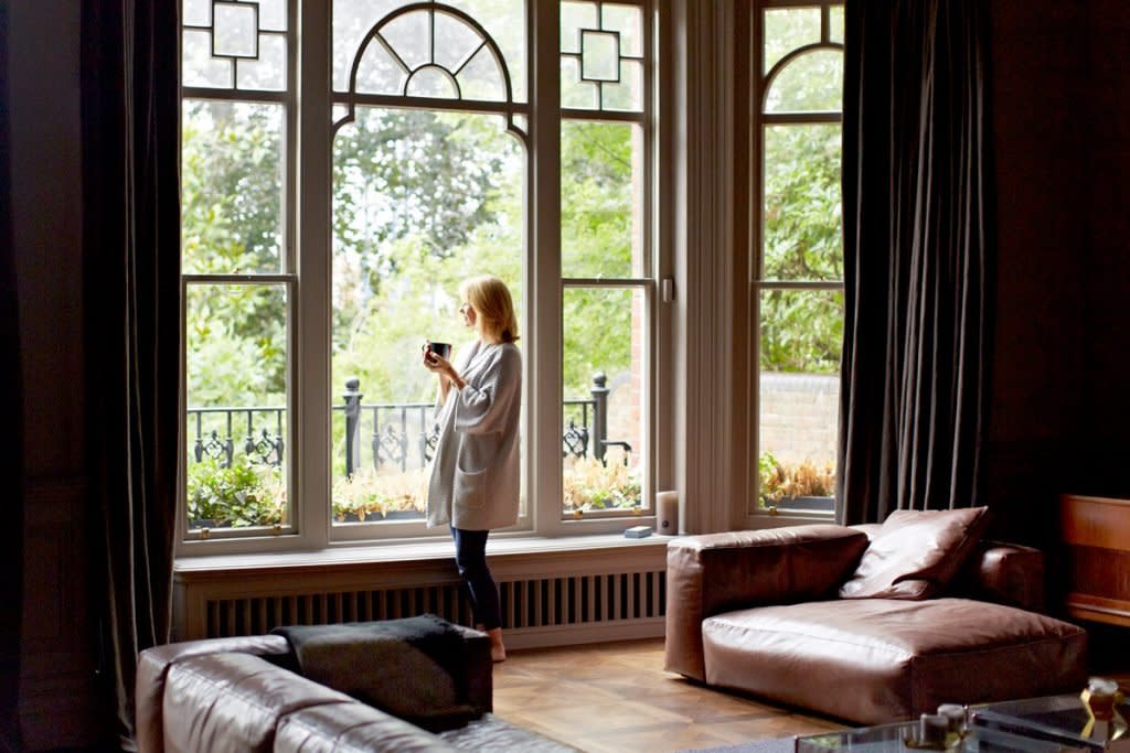 A woman looks out the window of her home while sipping coffee.