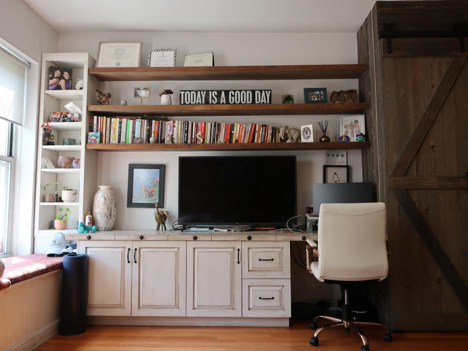 A TV on a desk with several book shelves overhead.