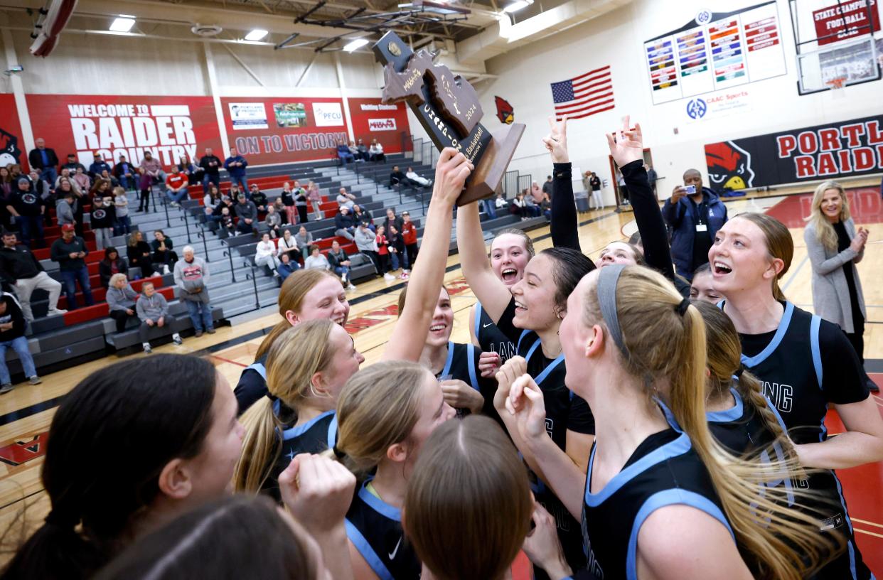 Lansing Catholic players celebrate with their District championship trophy after defeating Portland 56-37, Friday, March 8, 2024, at Portland High School.