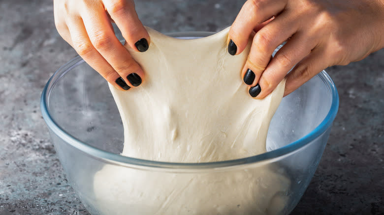 Woman's hands stretching dough out of bowl