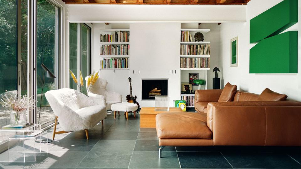 living room with sliding glass doors and love seat and matching chair at left, fireplace with bookshelves above left and right, leather couch at right with green artwork on wall above it