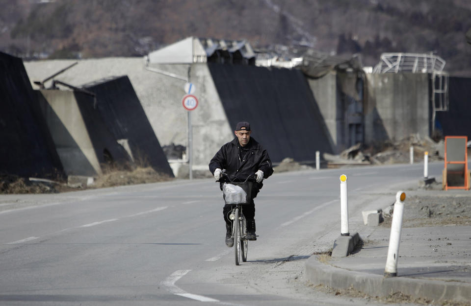 In this Tuesday, March 4, 2014 photo, a man pedals his bicycle by a breakwater, heavily damaged by the March 11, 2011 tsunami, awaiting reconstruction in Otsuchi, Iwate Prefecture, northeastern Japan. After three years of debate and red tape, many towns have settled on reconstruction plans, but shortages of skilled workers and materials are delaying the work. (AP Photo/Junji Kurokawa)