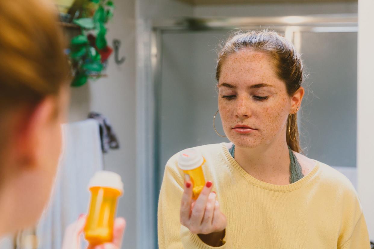 woman reading pill bottle label in bathroom