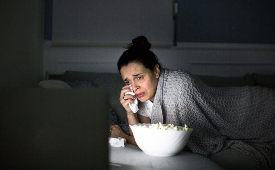 Woman watching TV with a bowl of popcorn, looking emotional