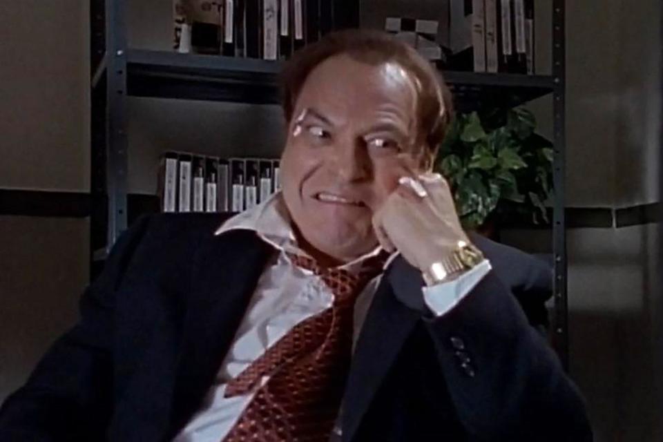 Rip Torn, in a suit and tie, grimaces and rests his head on his hand.