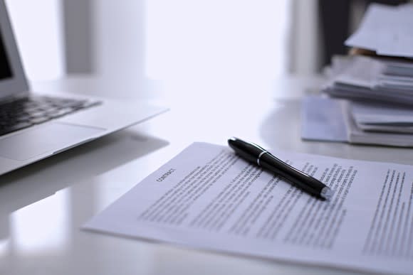 A contract and pen sitting on a desk.