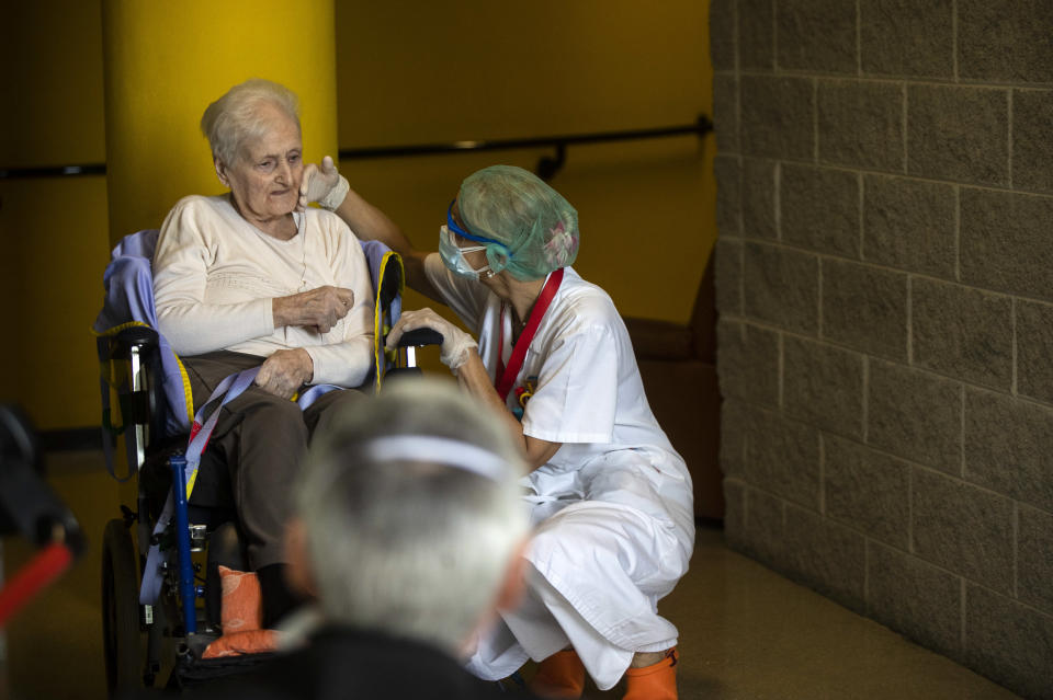 Maria Giulia Badaschi, health director, at the Martino Zanchi Foundation nursing home, strokes the face of Albina Minelli, 92, as she sits in a wheelchair and talks from a safe distance with her family in Alzano Lombardo, Italy, Friday, May 29, 2020. (AP Photo/Luca Bruno)