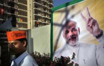 In this Tuesday, April 1, 2014, photo, a Bharatiya Janata party supporter stands in front of his prime ministerial candidate Narendra Modi poster at newly open election campaign office, in Varanasi, India. For tens of millions of Hindus, Varanasi is a place of pilgrimage. Crowded with ancient temples and shrines, its streets jammed with believers and tourists, this city on the banks of the holy Ganges River is where the devout believe they attain instant salvation. (AP Photo/Manish Swarup)