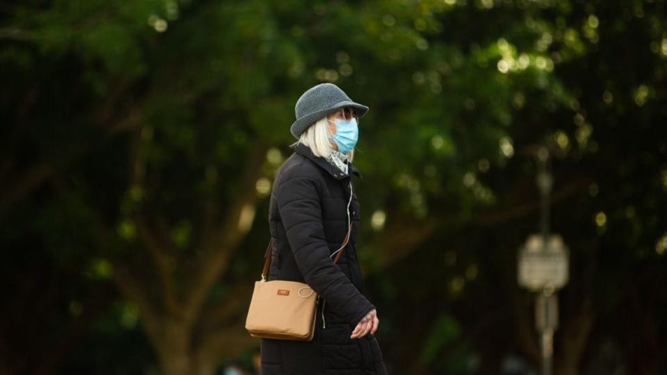 Woman wearing mask, coat and hat walking in Sydney during lockdown. 