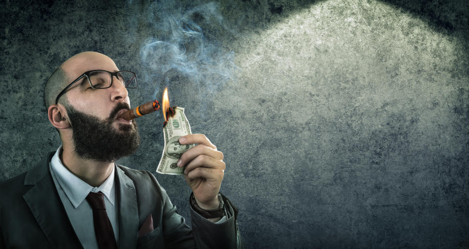 A man smokes a cigar by burning cash.