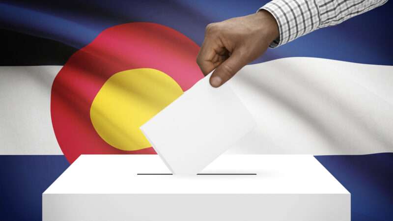 Voter casting a ballot in front of the Colorado state flag