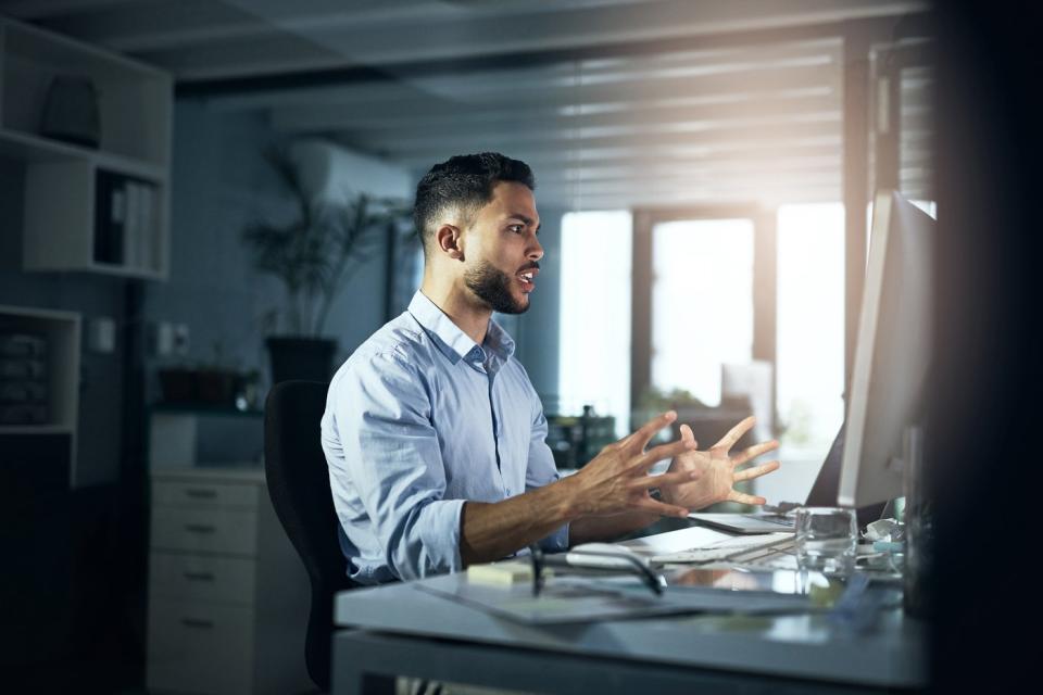 An angry person with his hands outstretched looking at a computer monitor.