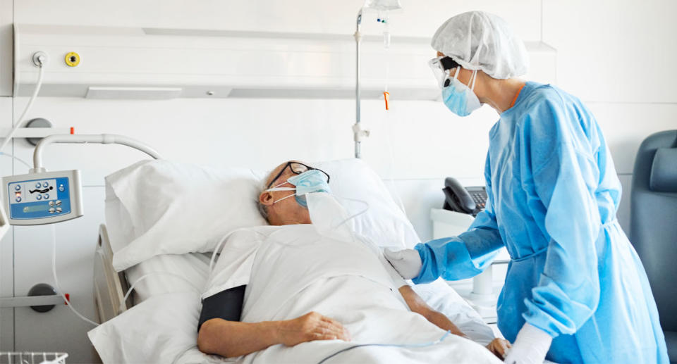 Man in hospital bed wearing mask with female doctor wearing protective clothing and mask