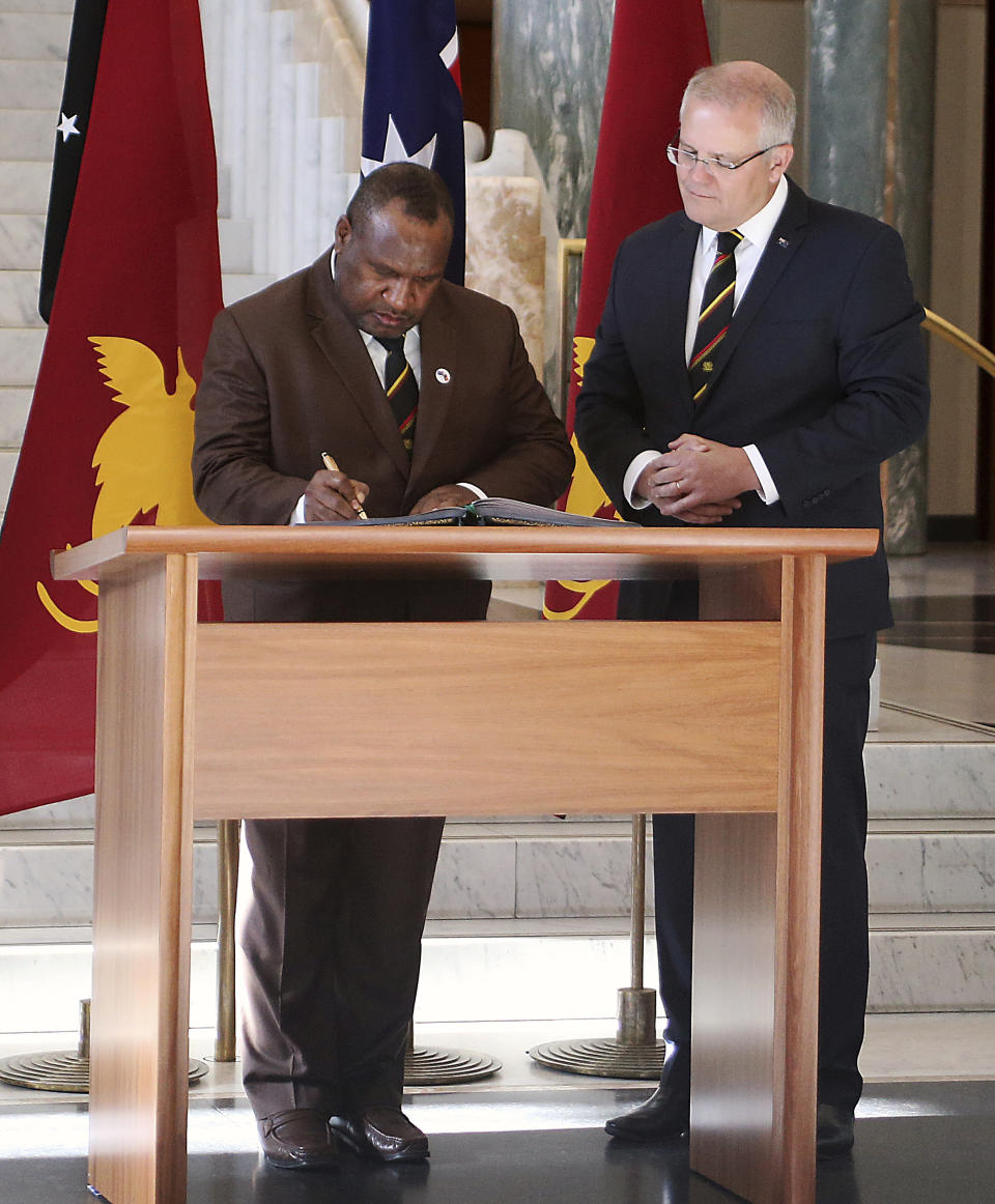 Papua New Guinea's Prime Minister James Marape, left, signs the visitors' book at Australia's Parliament House in Canberra watched by Australian Prime Minister Scott Morrison Monday, July 22, 2019. Marape says his country's relationship with China in not open to discussion during his current visit to Australia. (AP Photograph/Rod McGuirk)