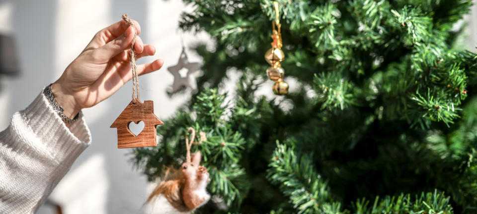 Person hanging wooden house-shaped ornament on a Christmas tree