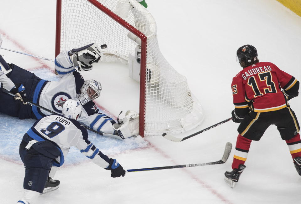 Winnipeg Jets goalie Connor Hellebuyck (37) is scored on by Calgary Flames' Johnny Gaudreau (13) as Jets' Andrew Copp defends during the second period of an NHL hockey playoff game Saturday, Aug. 1, 2020 in Edmonton, Alberta. (Jason Franson/The Canadian Press via AP)