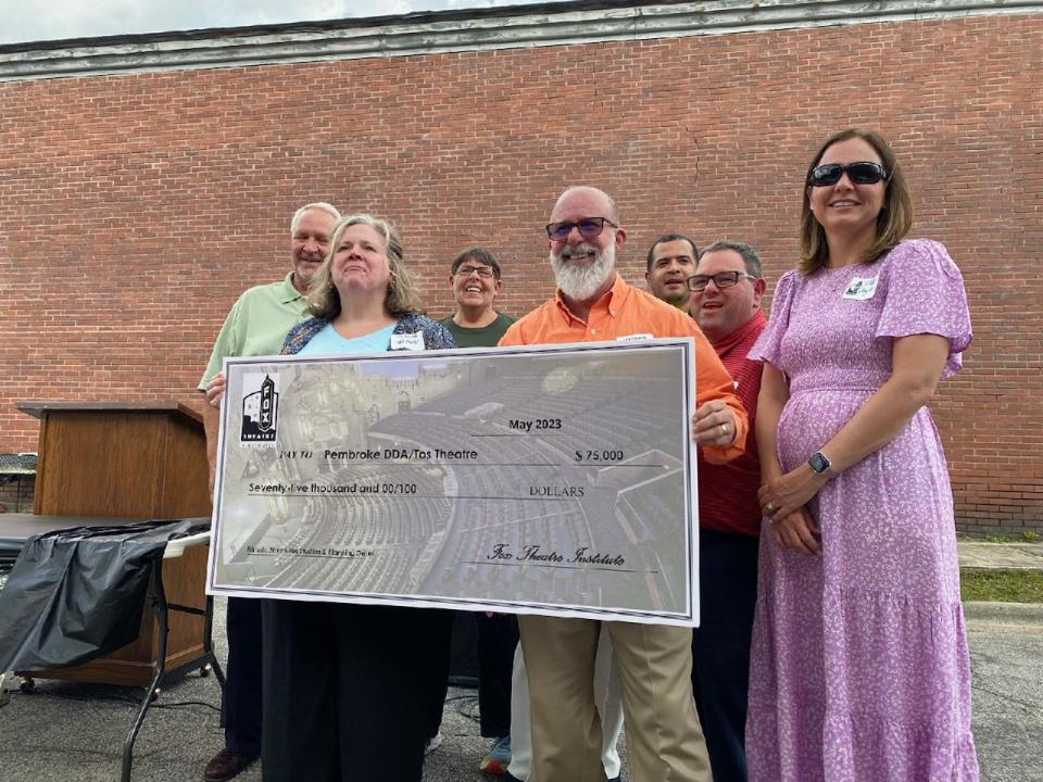 Board members of Friends of Tos Theatre are photographed celebrating a $75,000 donation presented by Leigh Burns (in blue) of the Fox Theatre Institute Tuesday in Pembroke. The funds will go towards renovations for the theater.