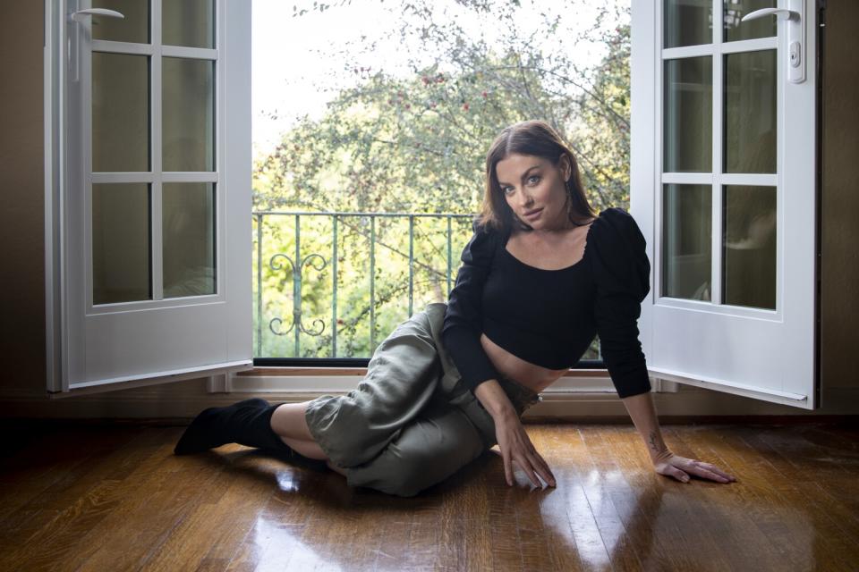 A woman sits on a hardwood floor in front of open French doors.