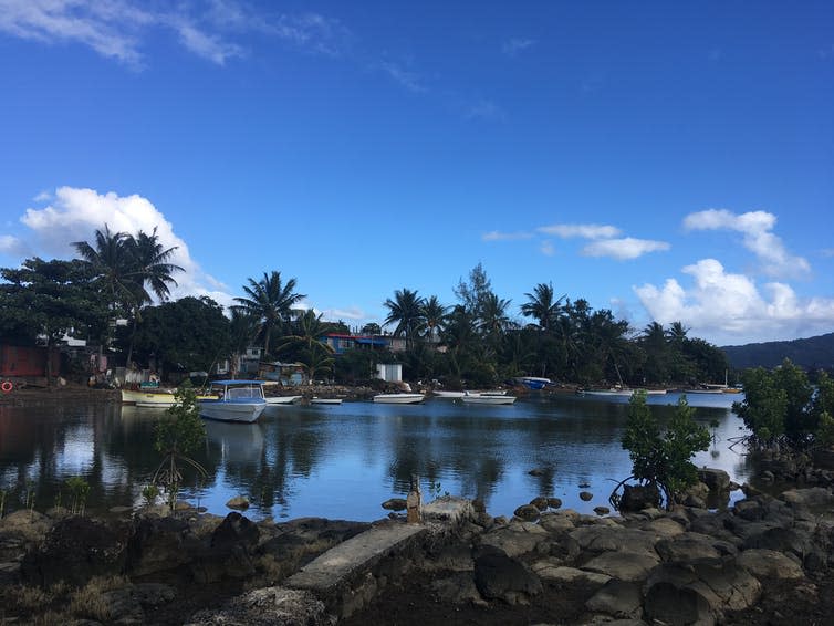 A tropical lagoon with trees in the background beneath a blue sky.