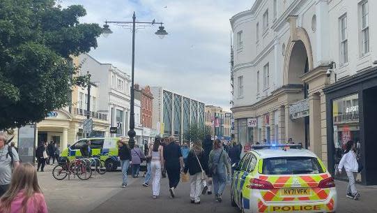 People walking past two parked police vehicles on Cheltenham High Street
