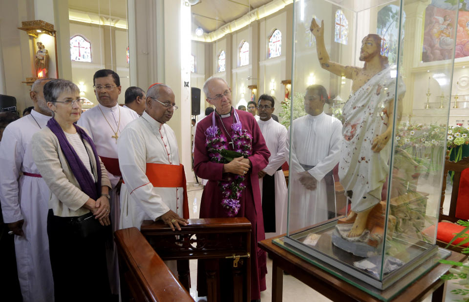 The Archbishop of Canterbury Justin Welby, with garland, looks at a blood-stained statue of Jesus Christ, along with the archbishop of Colombo Cardinal Malcolm Ranjith, fourth left, and the bishop of Colombo in the Church of Ceylon Dhiloraj Canagasabey, third left, at St. Sebastian's church in Katuwapitiya village, Negombo , Sri Lanka, Thursday, Aug. 29, 2019. The figurehead of the Church of England emphasized the need for Christian unity on Thursday as he paid tribute to the victims of the Easter Sunday bomb attacks at a Roman Catholic church in Sri Lanka. A total of 263 people were killed when seven suicide bombers from a local Muslim group attacked three churches and three luxury hotels on April 21. (AP Photo/Eranga Jayawardena)