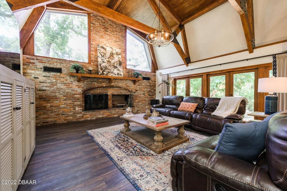 The great room features soaring ceilings with artistically placed wood beams and accents, a wood-burning fireplace and French Doors leading to one of the brick-paver patios.