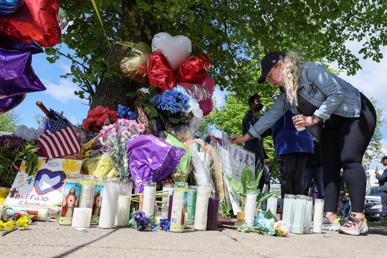 A woman visits a sidewalk memorial of flowers, balloons and candles for the Buffalo shooting victims.