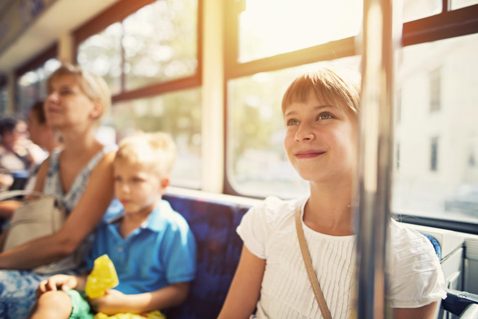 Smiling little girl aged 9 travelling by bus with mother and brother. They girl is smiling, summer sun is shining through the bus window. Mother and brother in the background.