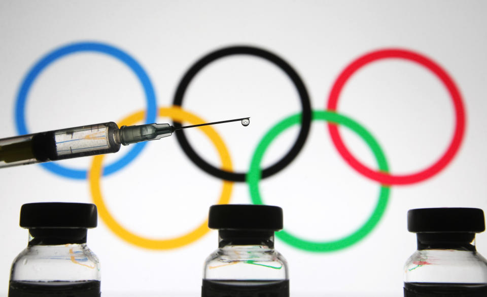 UKRAINE - 2021/01/01: In this photo illustration a medical syringe and vials are seen in front of the Olympic Games rings. #The World Health Organization (WHO) on 31 December 2020 lists Pfizer/BioNTech vaccine for emergency use, as media reported. (Photo Illustration by Pavlo Gonchar/SOPA Images/LightRocket via Getty Images)