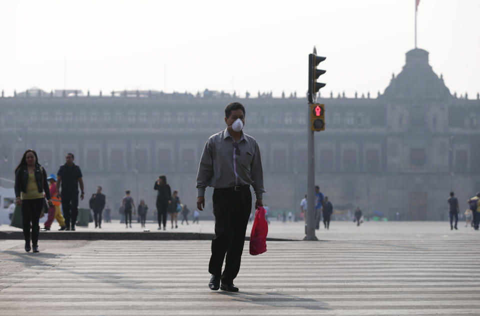 A man wearing a face mask crosses a street backdropped by the National Palace shrouded by haze, in the Zocalo, Mexico City's main square, Thursday, May 16, 2019. A siege of air pollution blanketing the capital has led to school closures and the cancellation of professional sporting events. (AP Photo/Rebecca Blackwell)