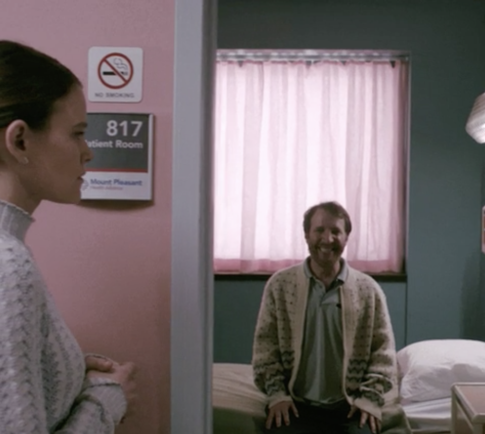 A man sitting on the side of his bed in a doctor's office with a big grin on his face