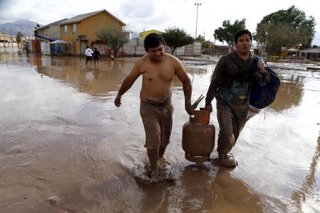 Locals carry a gas bottle on a flooded street at Copiapo city, March 26, 2015. REUTERS/Ivan Alvarado