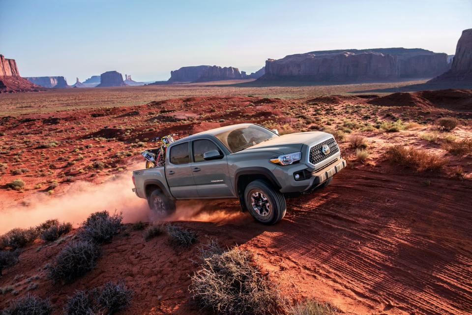 A gray Toyota Tacoma truck driving up red sand and rocks.