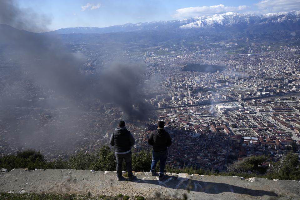 FILE - Two men watch the smoke rising from a building in Antakya, southern Turkey, Feb. 8, 2023. A year after the devastating 7.8 magnitude earthquake struck southern Turkey and northwestern Syria, a massive rebuilding effort is still trudging along. The quake caused widespread destruction and the loss of over 59,000 lives. (AP Photo/Khalil Hamra, File)