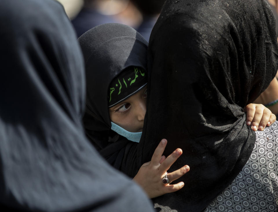 A young Kashmiri Shiite Muslim watches a Muharram procession, cradled in the arms of a woman in Srinagar, Indian controlled Kashmir, Saturday, Aug. 29, 2020. Muharram is a month of mourning in remembrance of the martyrdom of Imam Hussein, the grandson of Prophet Mohammed. Authorities had imposed restrictions in parts of Srinagar, the region's main city, to prevent gatherings marking Muharram from developing into anti-India protests. (AP Photo/Mukhtar Khan)