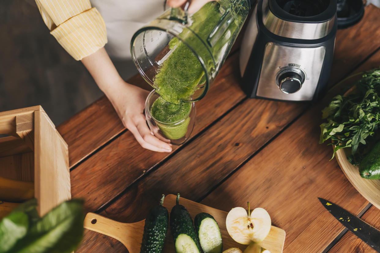 A woman pouring green vege and fruit juice from mixer into glass in kitchen. (PHOTO: Getty Images)