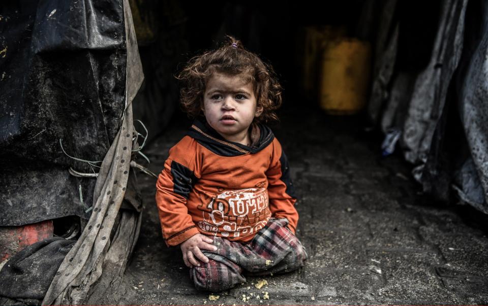 Palestinian child sits near a makeshift tent in Rafah